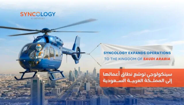A blue helicopter piloted by a robot flying over a Saudi Arabian city skyline, pulling a banner that reads Syncology expands operations to the Kingdom of Saudi Arabia.
