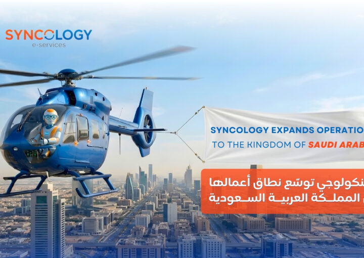 A blue helicopter piloted by a robot flying over a Saudi Arabian city skyline, pulling a banner that reads Syncology expands operations to the Kingdom of Saudi Arabia.