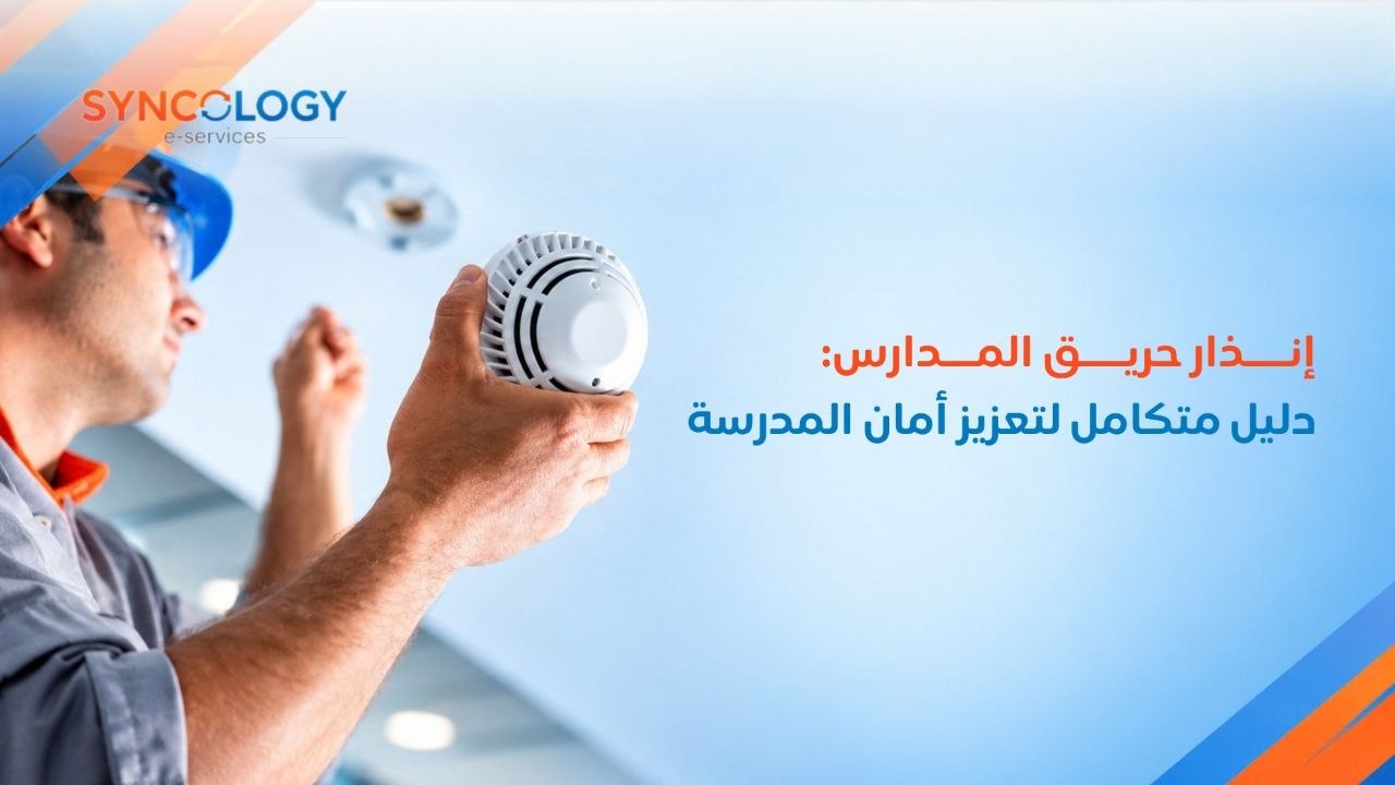 فني صيانة يرتدي خوذة زرقاء يقوم بتثبيت كاشف الدخان والسخونة بالسقف كجزء من نظام إنذار حريق المدارس.